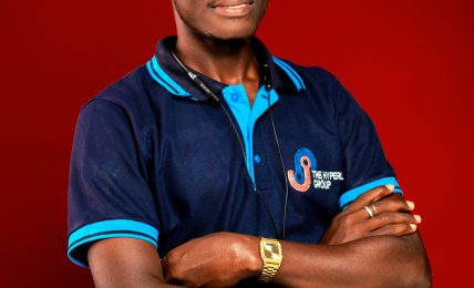 Young man with arms crossed, wearing a navy blue polo shirt with blue accents, standing against a red background.