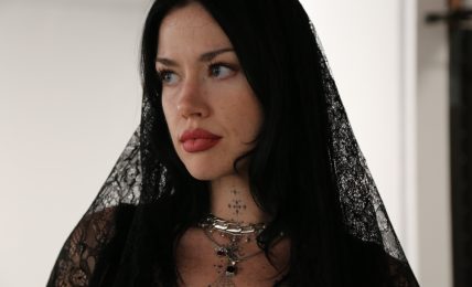 Woman with long black hair wearing black lace veil and jewelry, looking to the side, indoors.