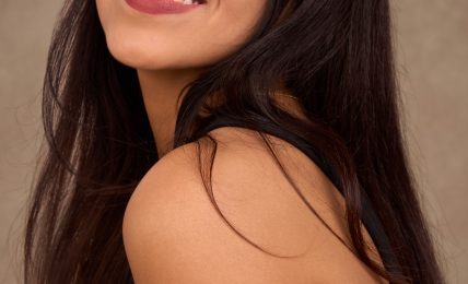 Young woman with long dark hair smiling, wearing a black top, against a neutral background.