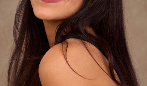 Young woman with long dark hair smiling, wearing a black top, against a neutral background.