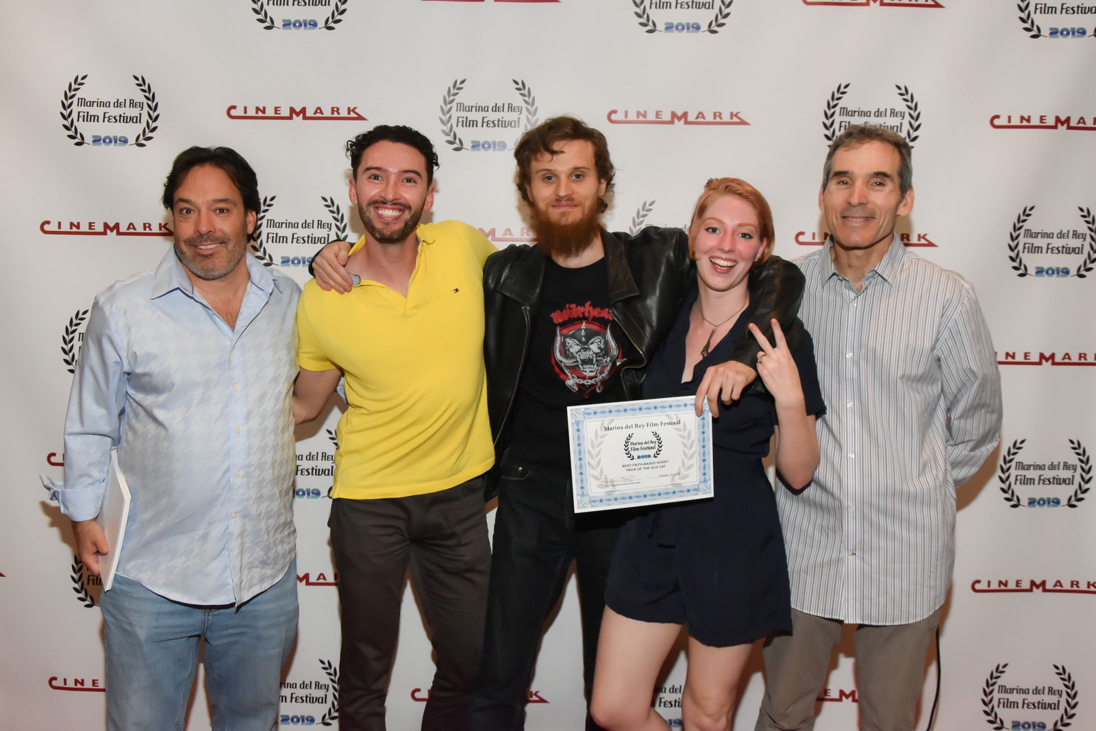 Group of five people smiling, one holding a certificate, standing in front of a backdrop with logos.