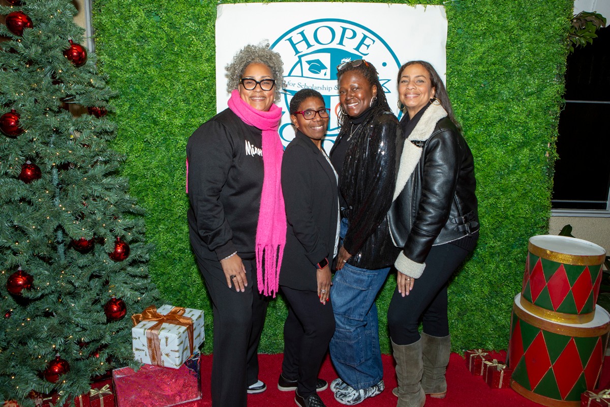 Four women stand in front of a green backdrop with a Hope logo, smiling, with Christmas decorations nearby.