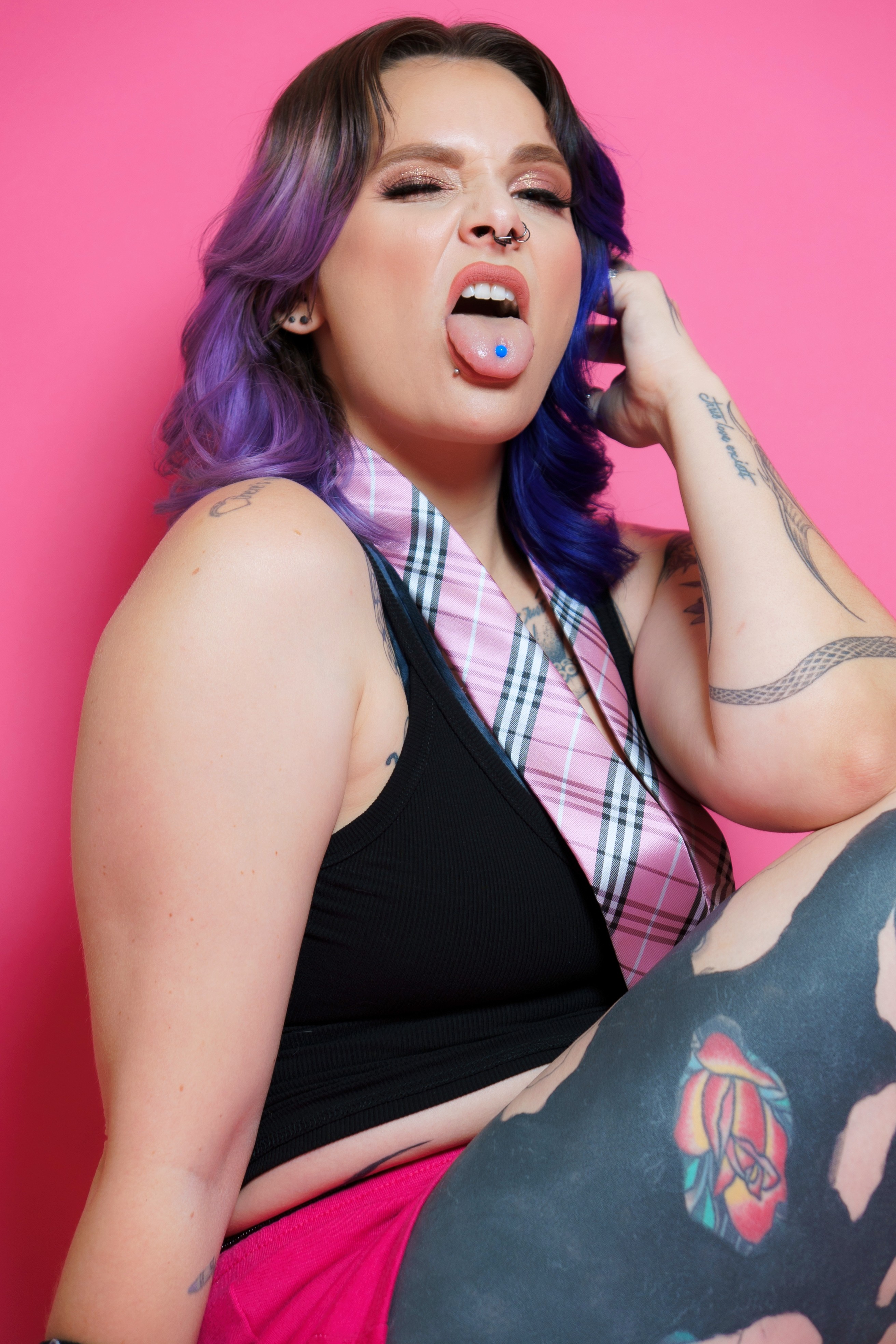 Woman with purple and blue hair, making a rebellious expression, against a pink background.