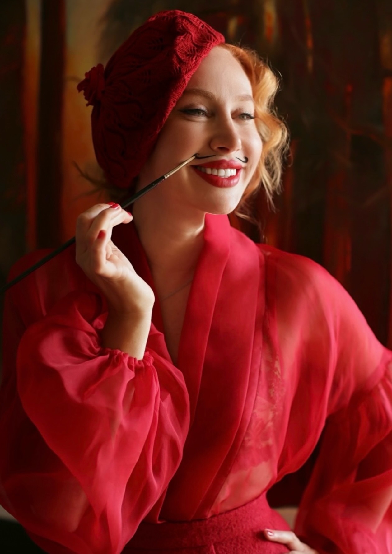 Woman with red hair and lipstick, wearing a red silk robe, smiling and holding a cigarette holder.
