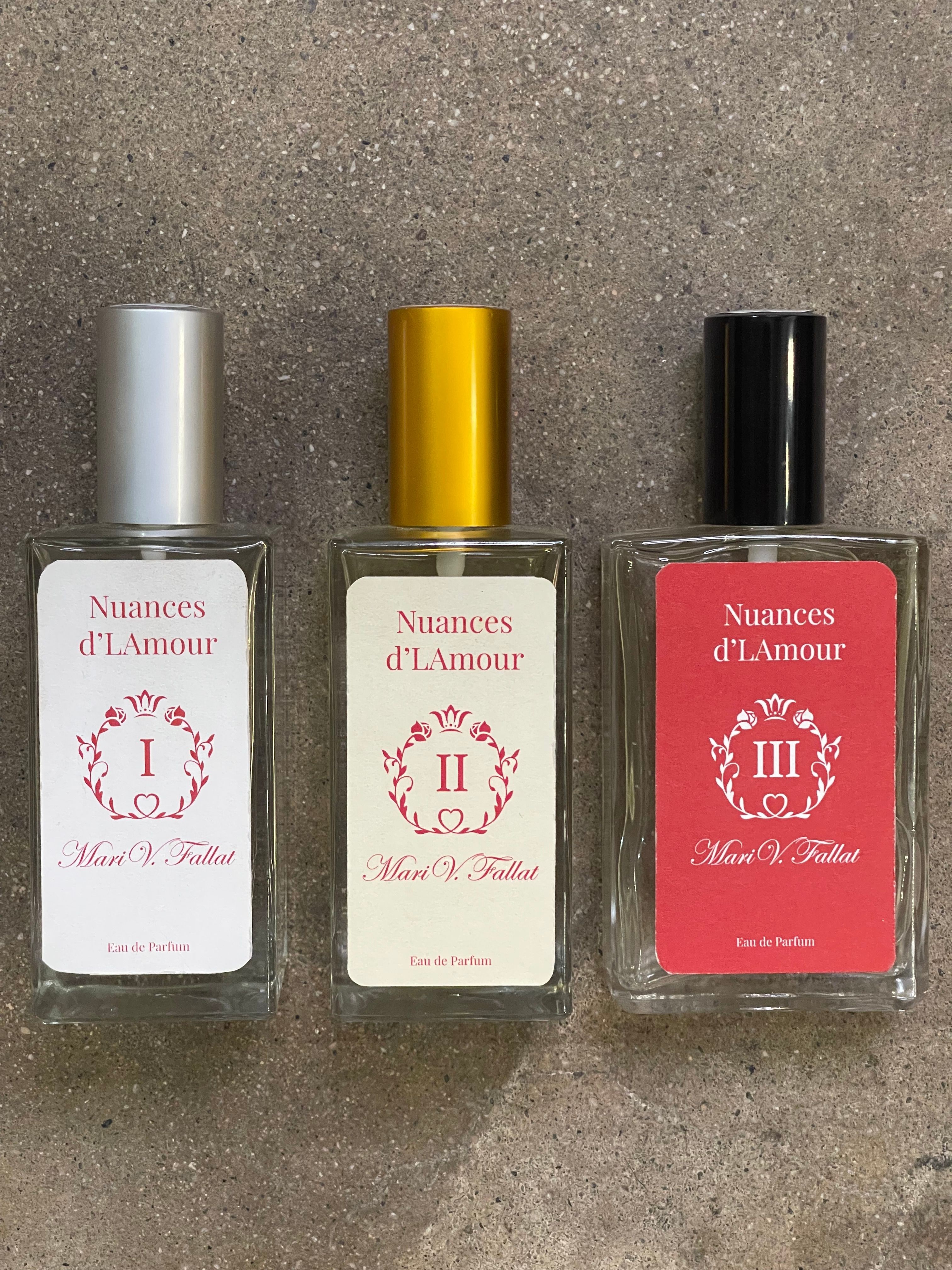 Three bottles of perfume or cologne with black, gold, and silver caps, arranged horizontally on a gray surface.