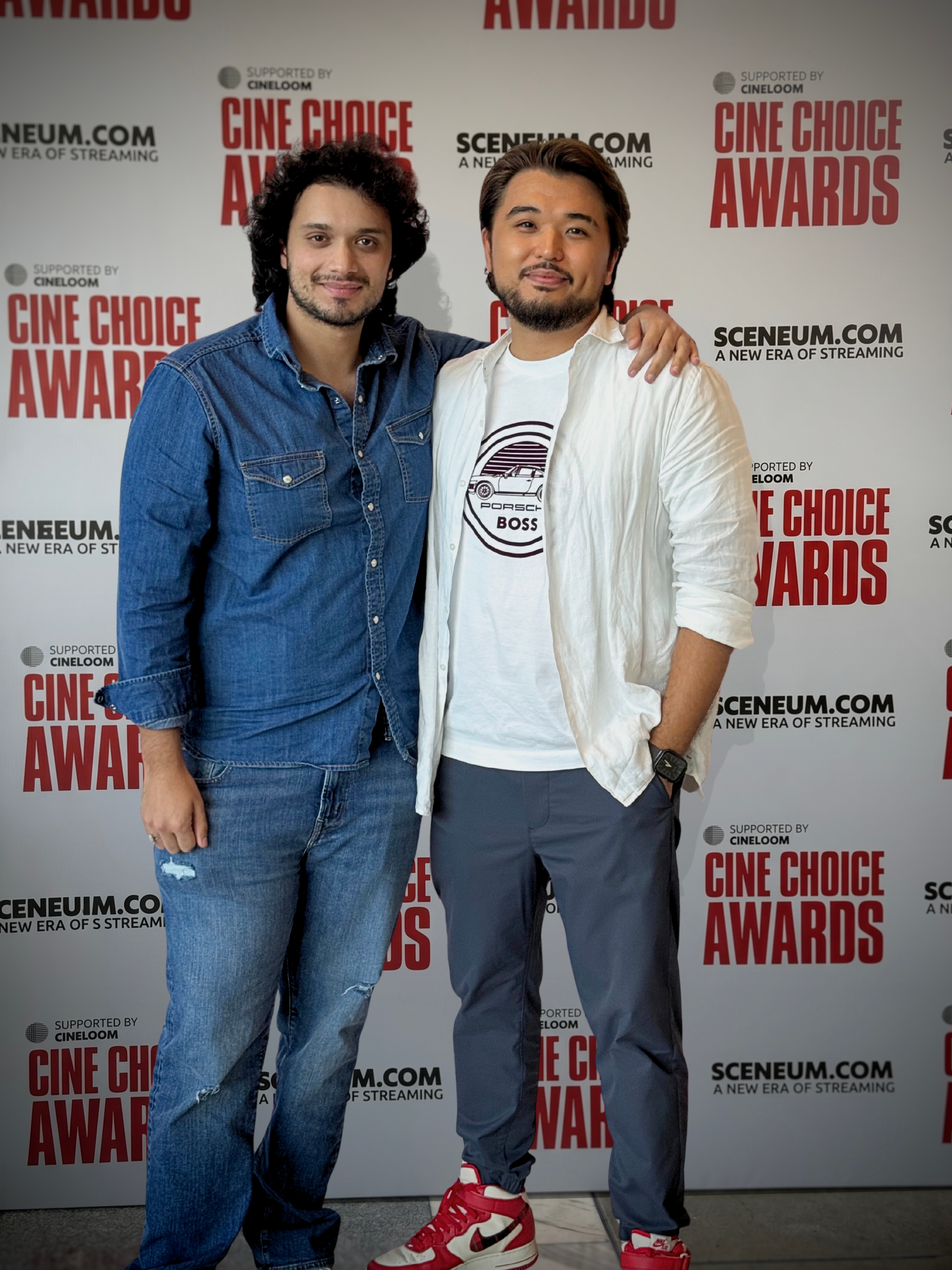 Two men standing together at an event, smiling, with a backdrop displaying 'Cine Choice Awards' and related logos.
