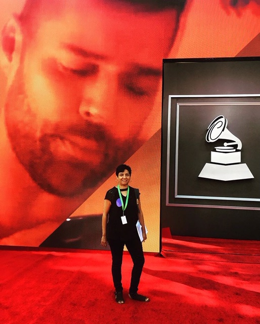 Person standing on red carpet in front of large screen with a record player icon, large face image in background.