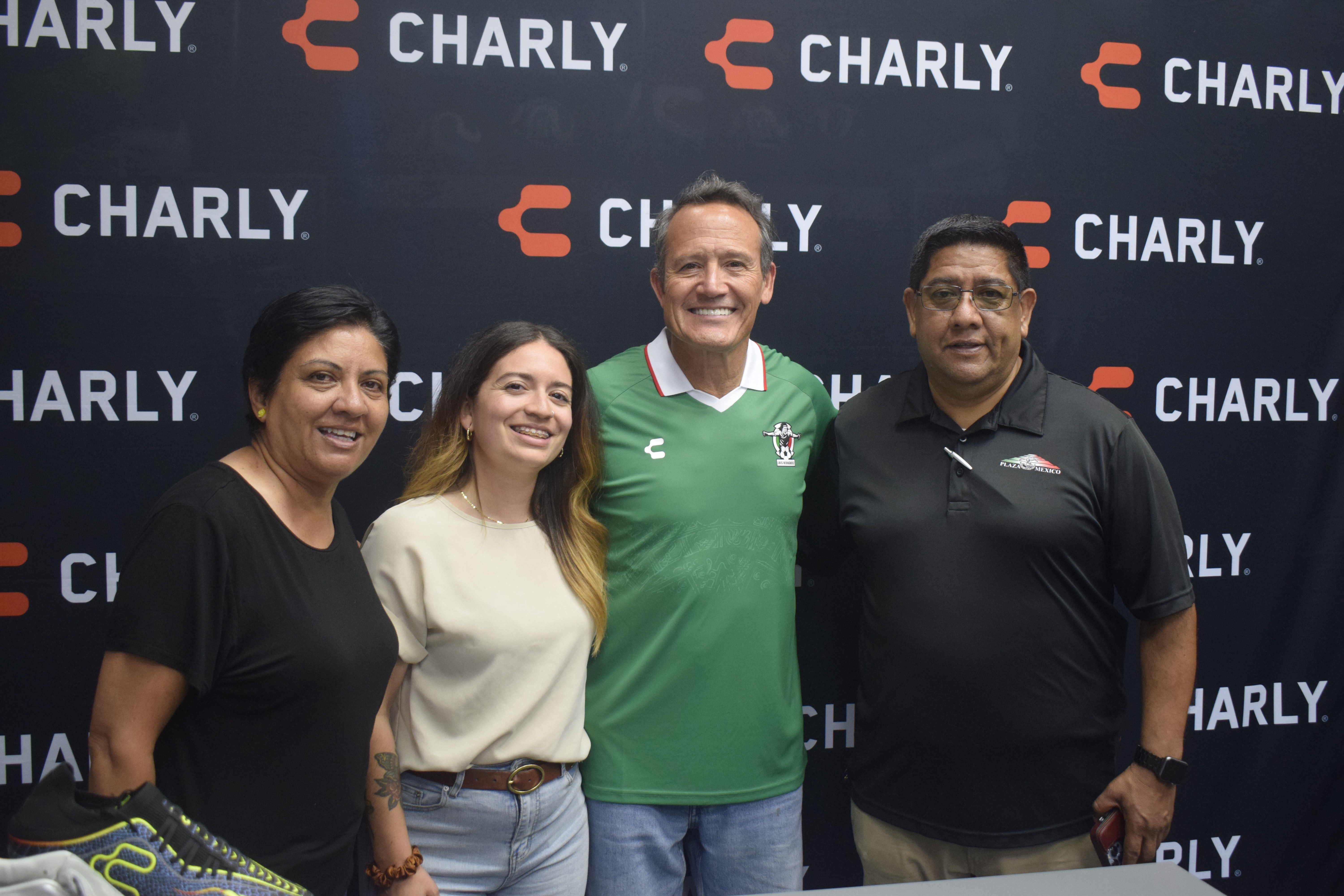 Four people standing in front of a black backdrop with the word 'CHARLY' repeated, smiling for the photo.