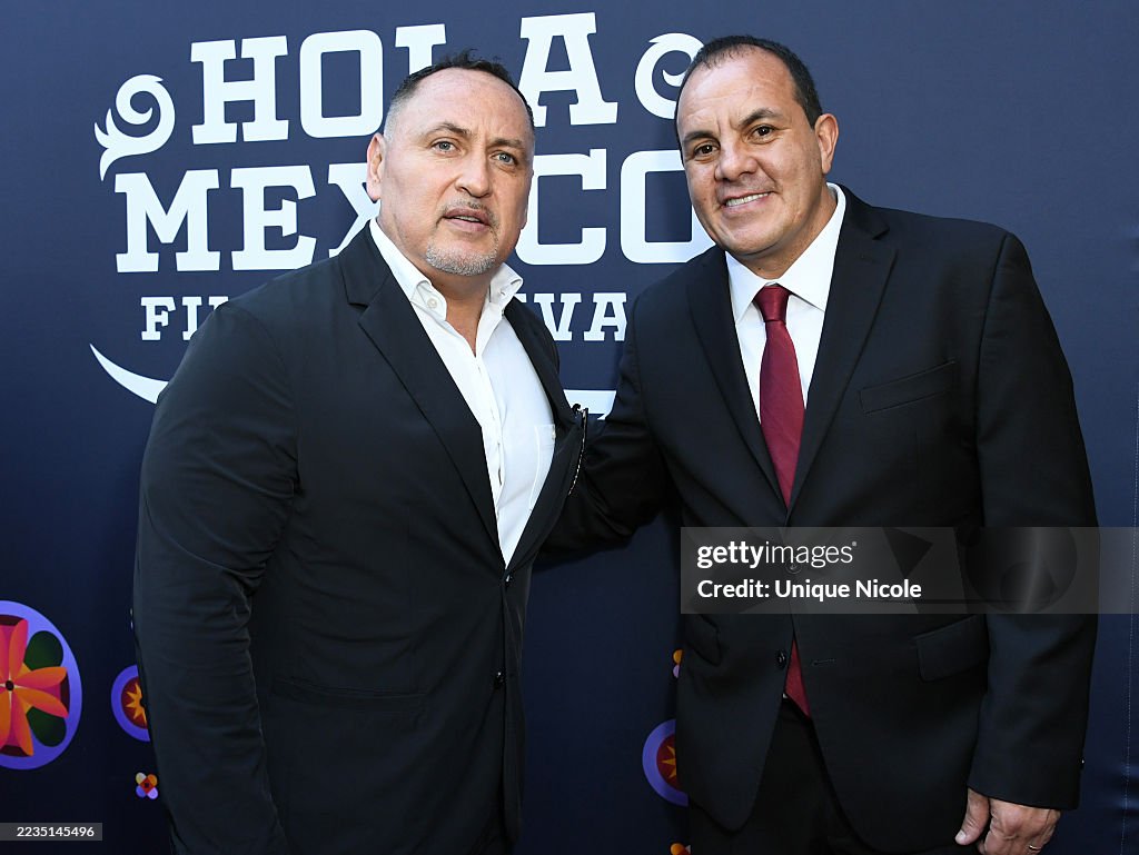 Two men in suits standing together in front of a blue background with text, smiling at the camera.