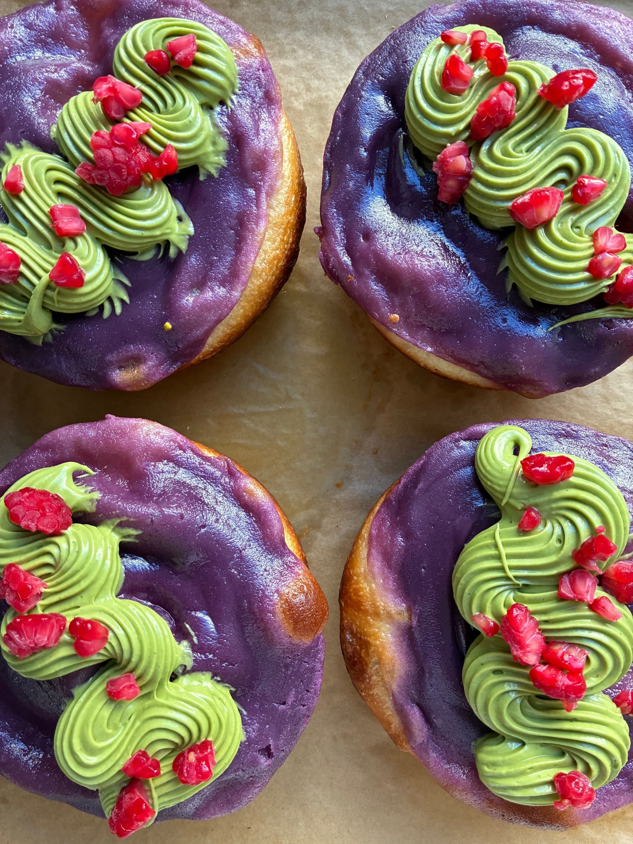 Four donuts with purple glaze, topped with green frosting and red sprinkles, on a brown surface.