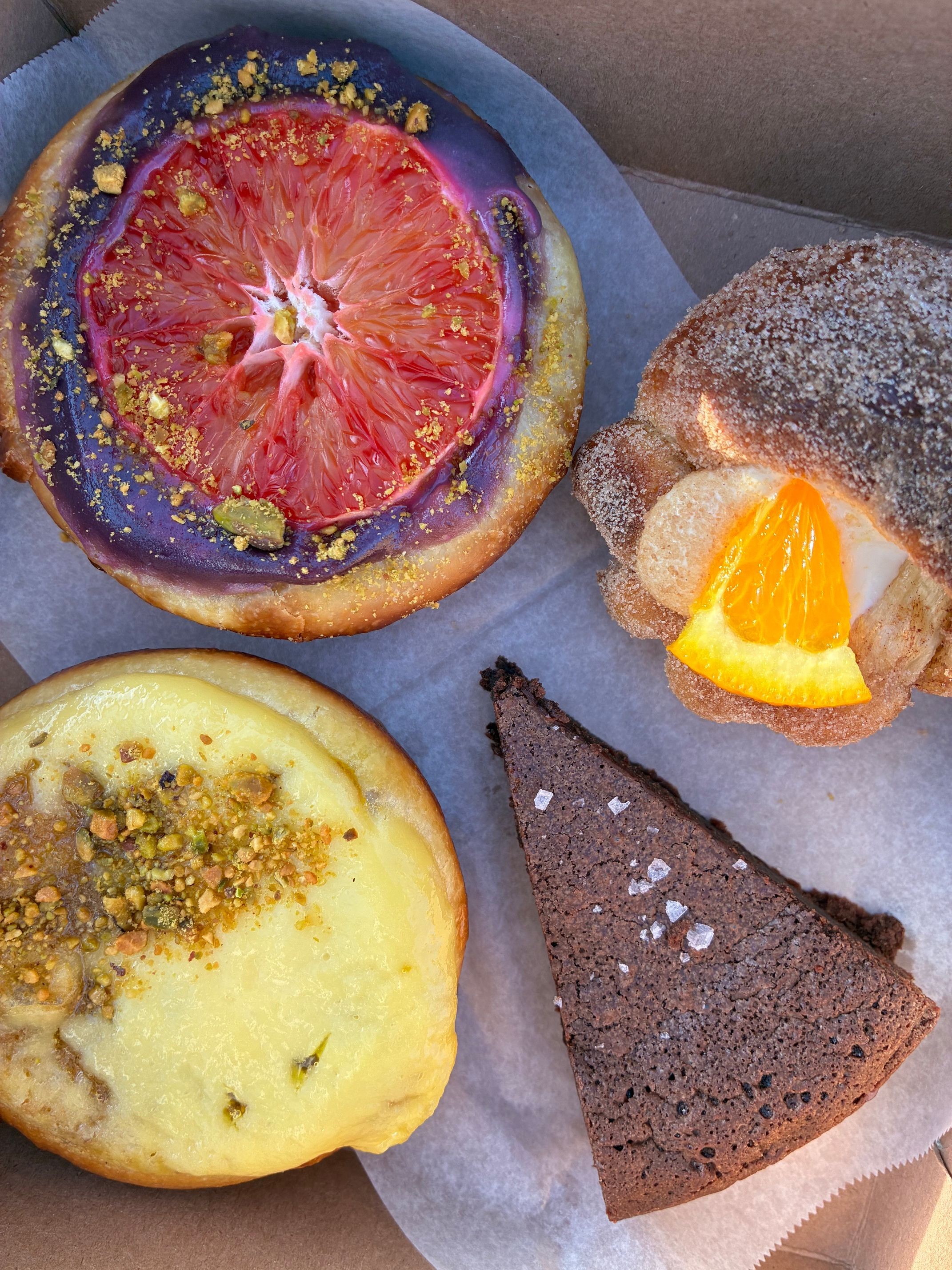 Four different slices of cake and a fruit tart on parchment paper, including a chocolate cake, a fruit tart, and two other cake slices.
