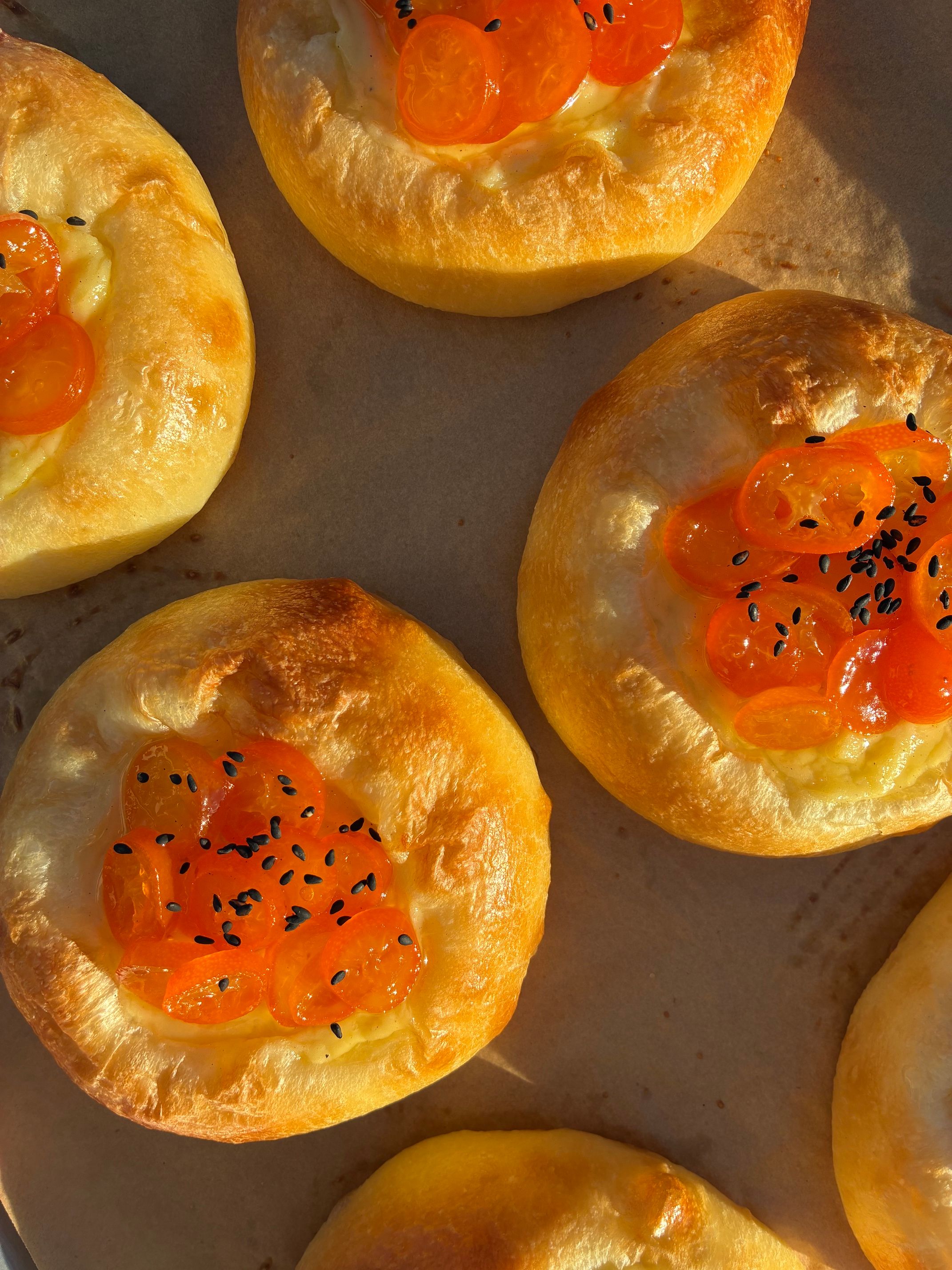Mini bread rolls topped with orange fish roe and black sesame seeds, on a baking sheet.