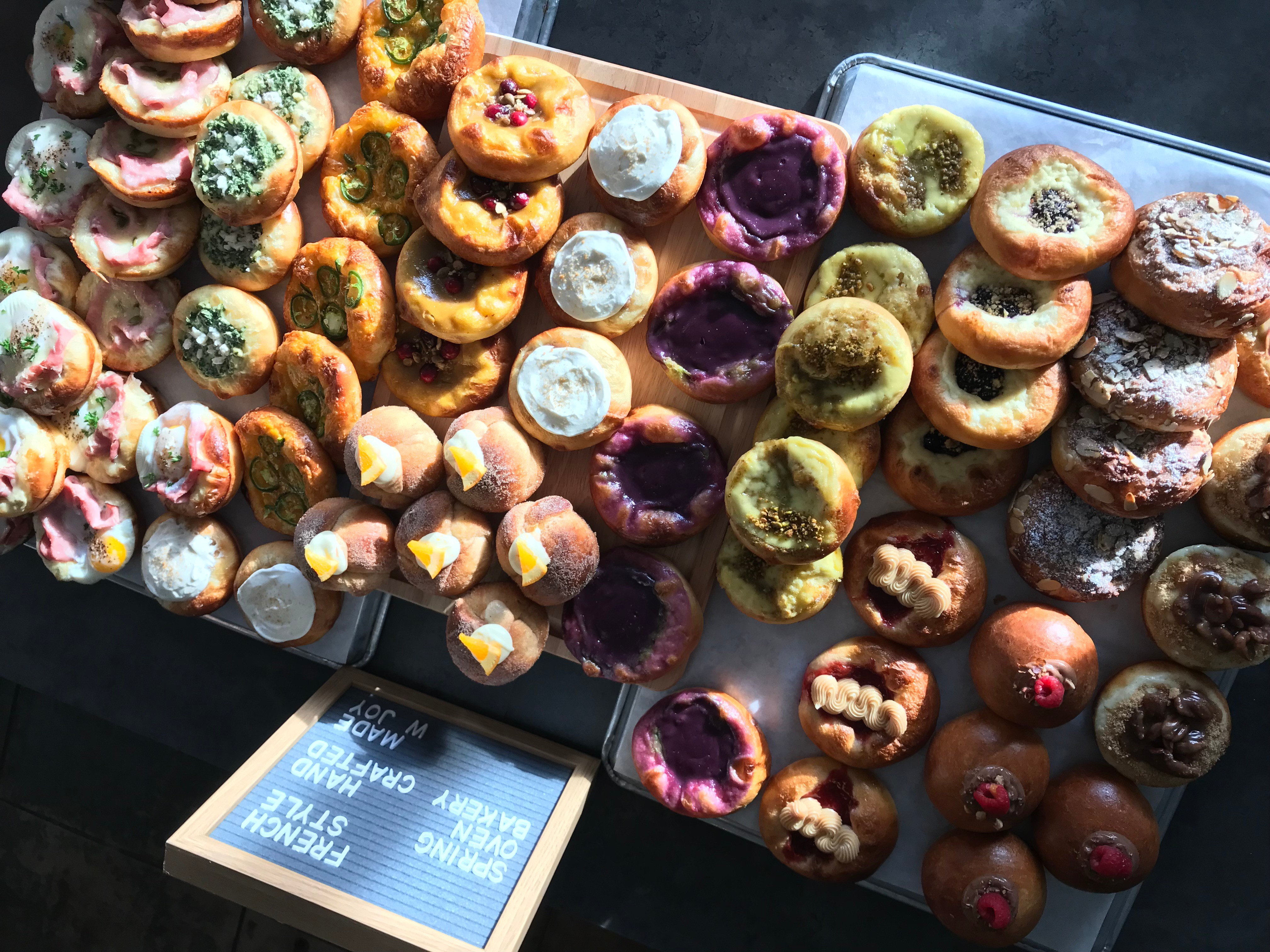 Assorted colorful mini donuts arranged on trays, some with icing, sprinkles, or toppings, in bright lighting.
