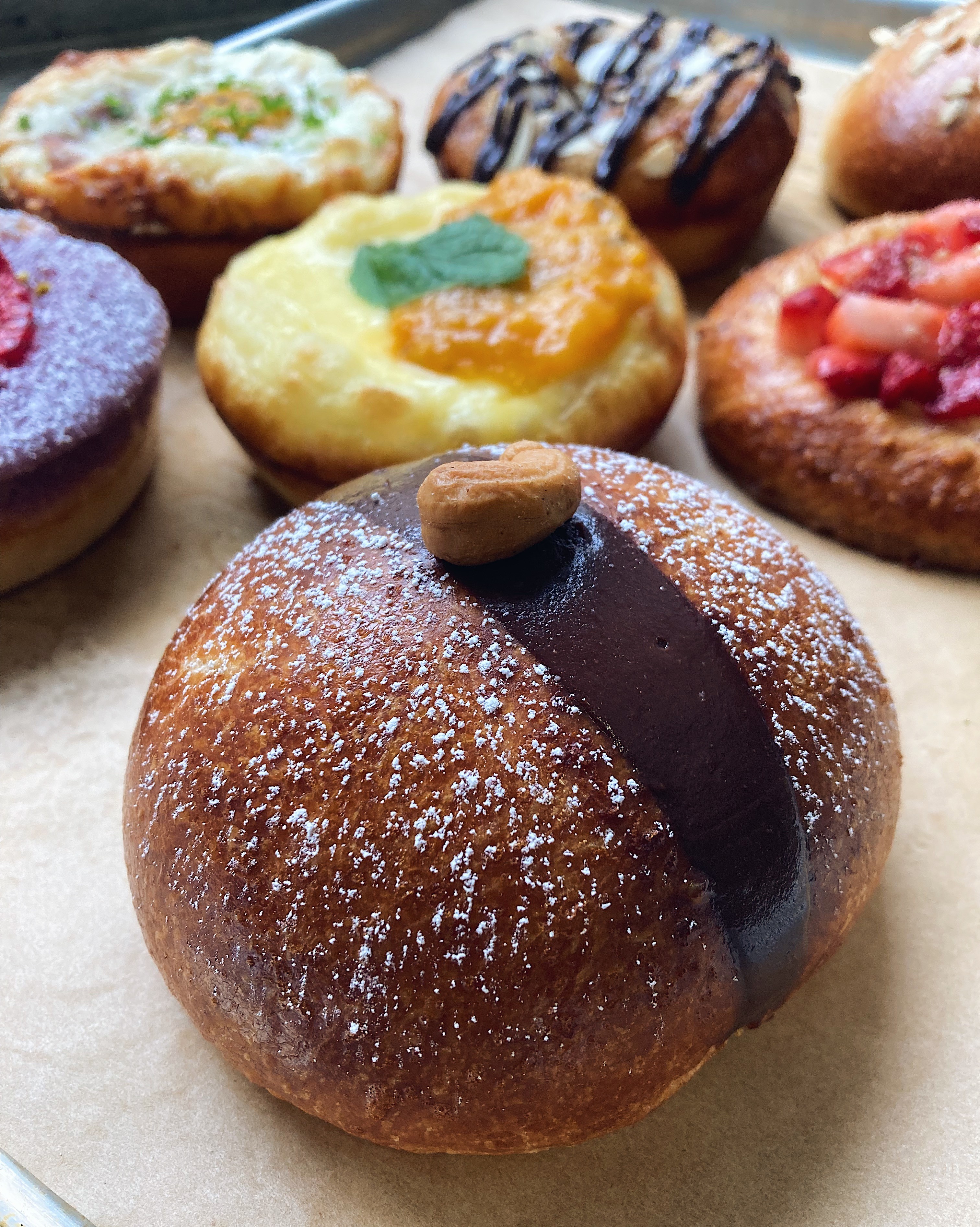 Assorted donuts with various toppings and fillings, including chocolate, fruit, and icing, on a paper surface.