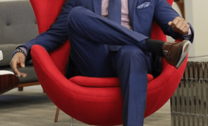 Man in a blue suit sitting in a red modern chair with a high back, in an office setting.