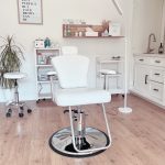 Medical or beauty treatment room with a white chair, shelves, and a lamp, on a wooden floor.