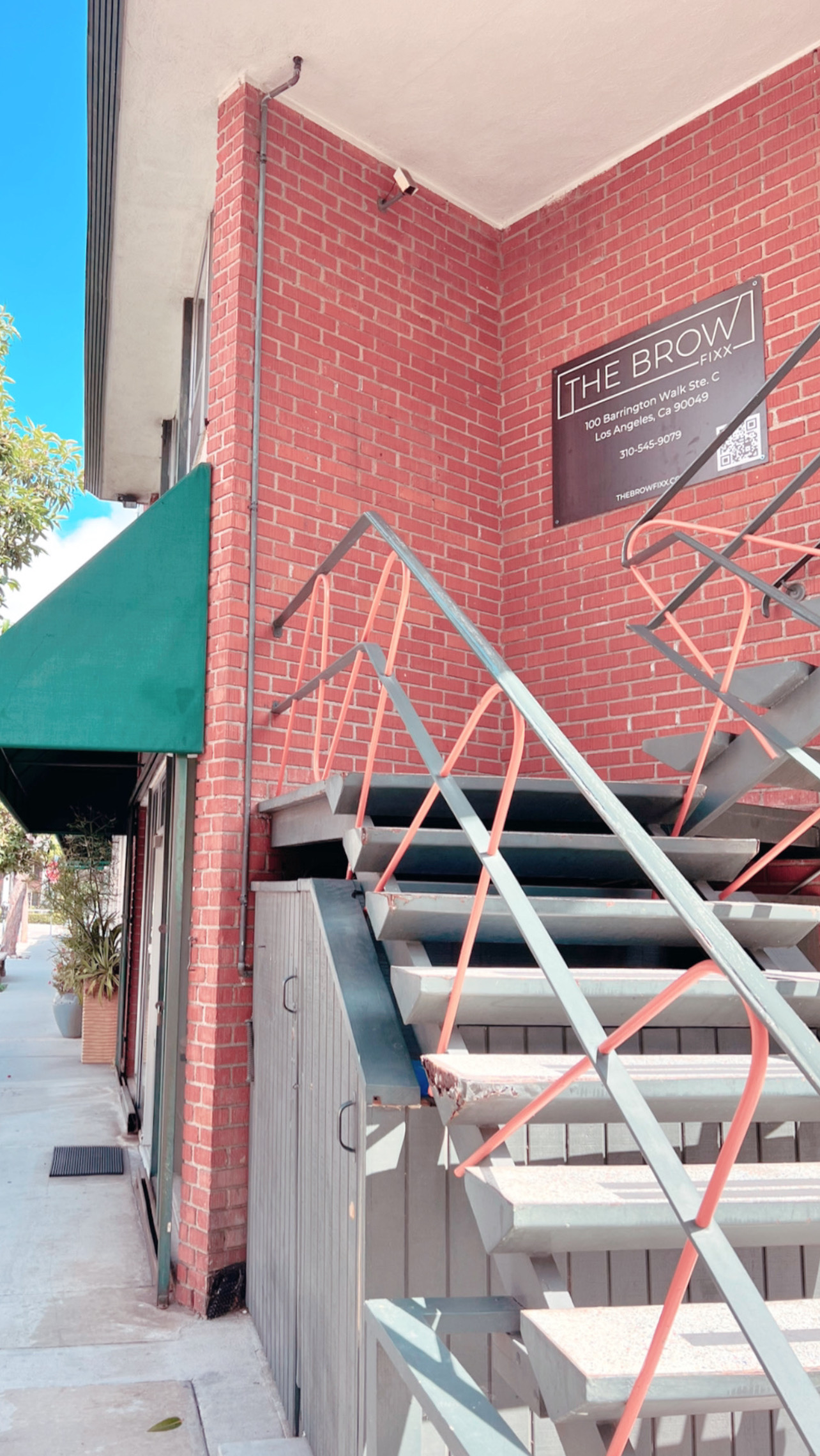 Brick building with stairs and a sign reading 'The Brow' on the wall, with a green awning on the side.
