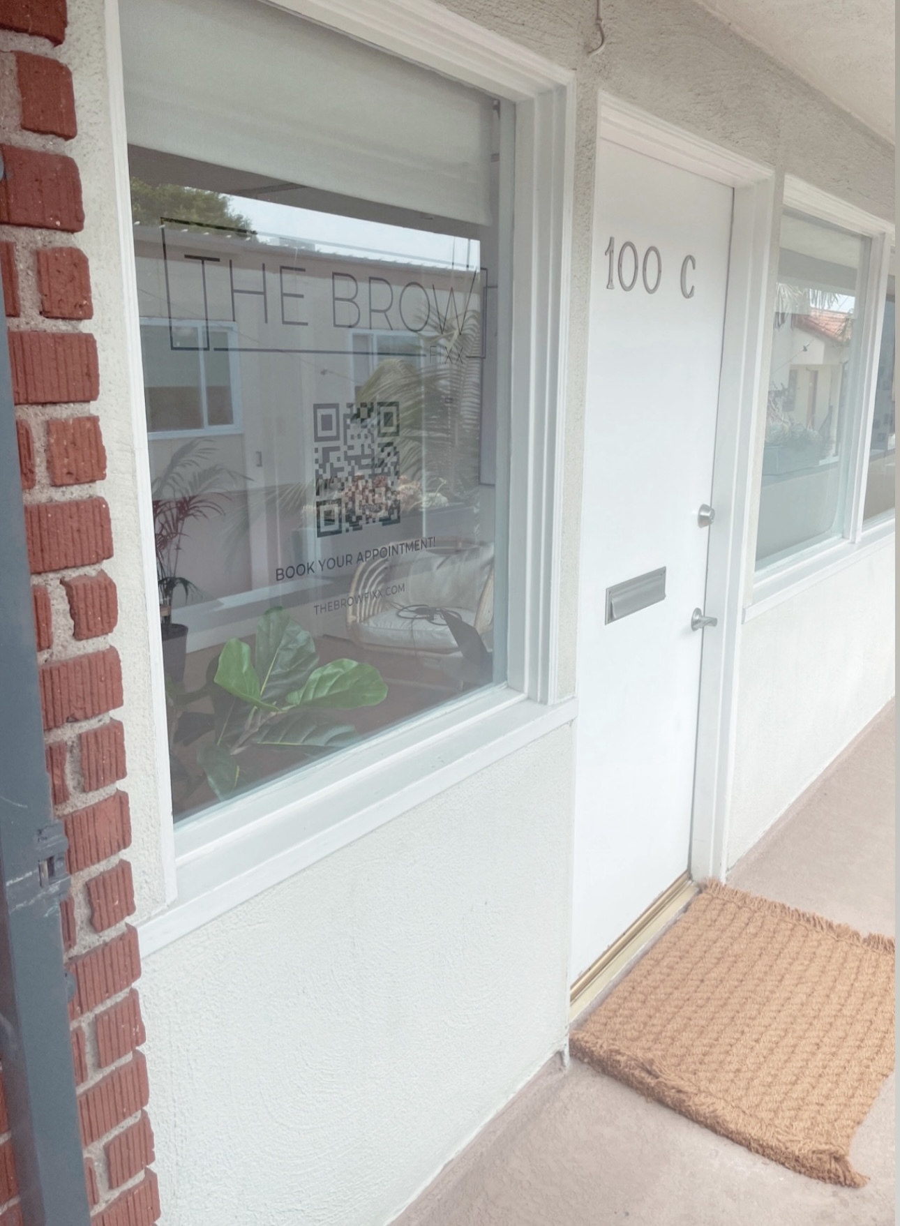 White door with address number 100 C and a window, outside a building with a doormat in front.