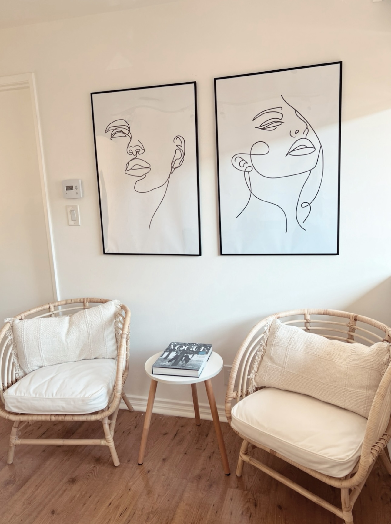 Two framed line art portraits of women hang on a wall above two armchairs and a small table.