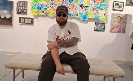 Person sitting on a bench in an art gallery with colorful paintings and framed pictures on the wall behind.