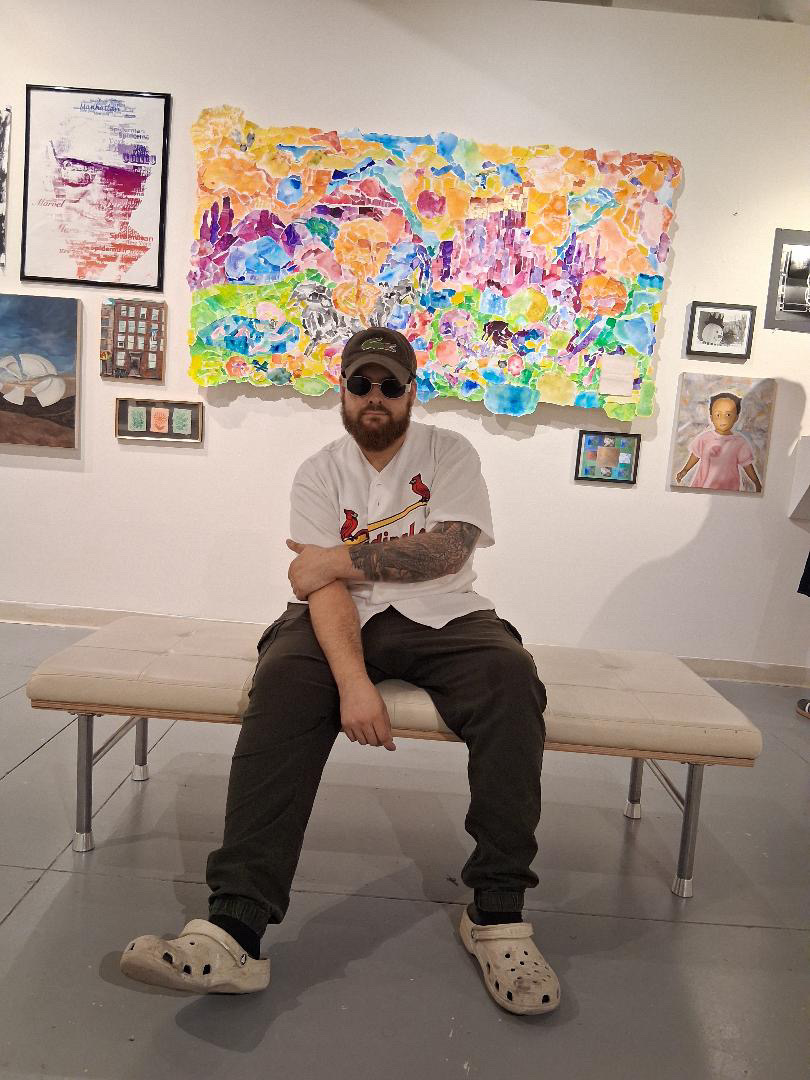 Person sitting on a bench in an art gallery with colorful paintings and framed pictures on the wall behind.