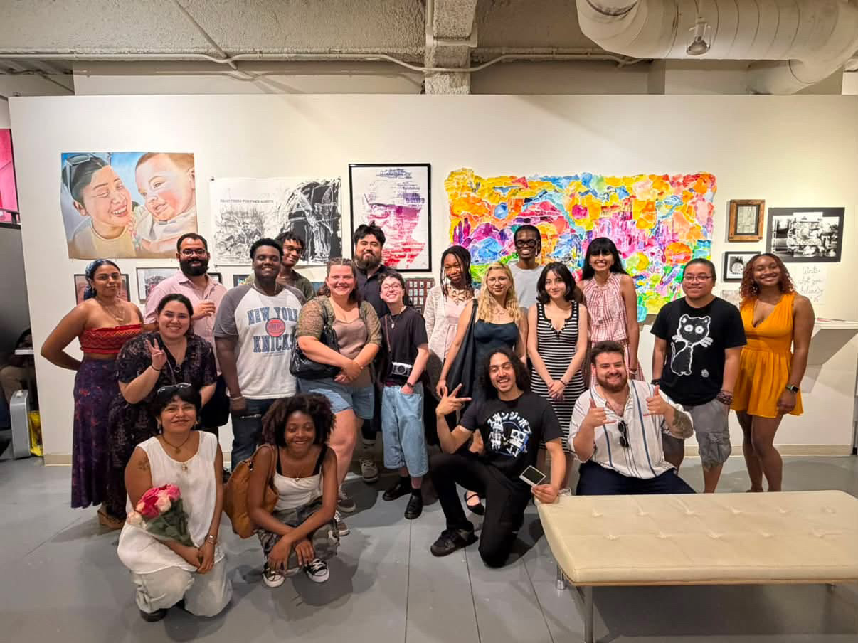 Group of people posing in an art gallery with colorful paintings and photographs on the wall behind them.