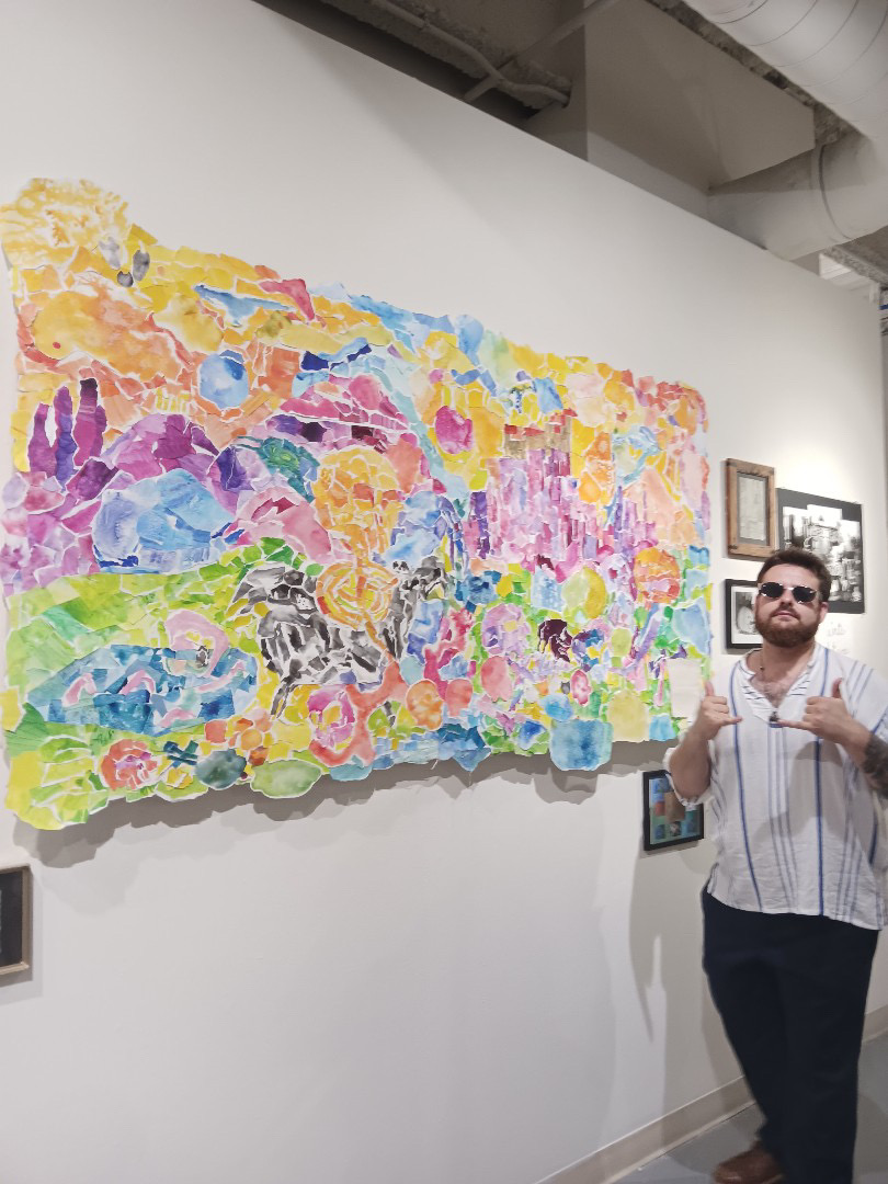 Person with sunglasses and striped shirt standing next to colorful abstract painting on gallery wall.