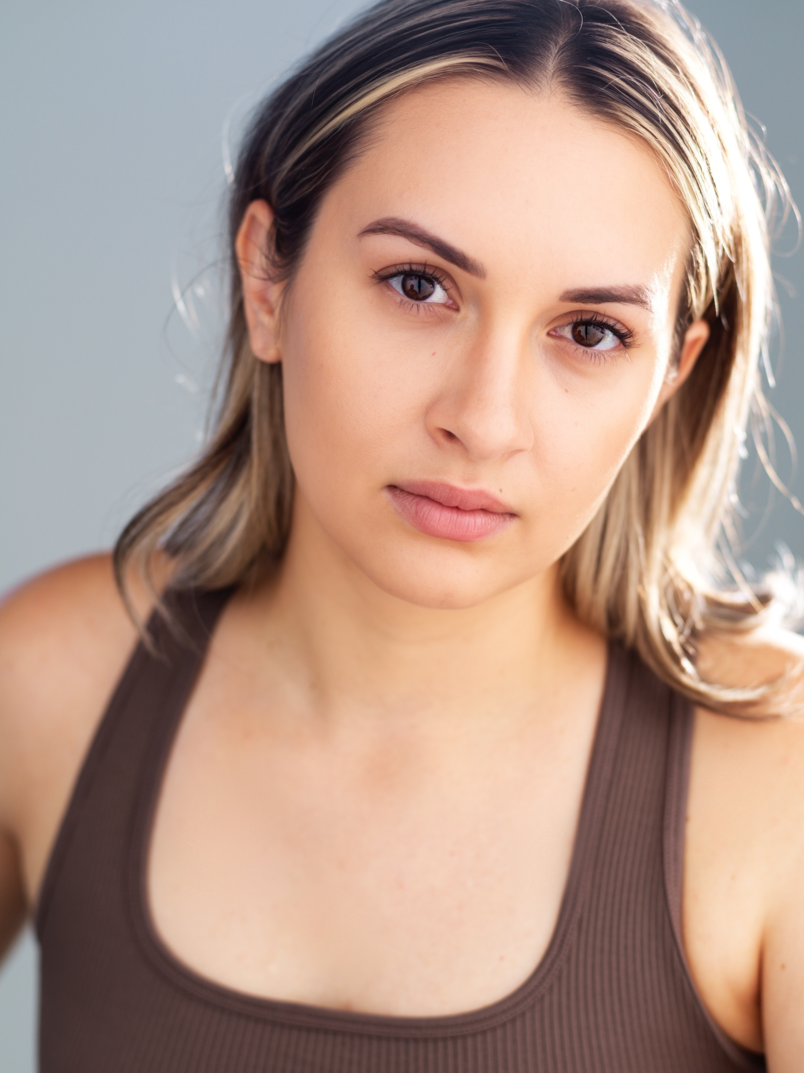 Young woman with light skin and blonde hair, wearing a dark tank top, looking directly at the camera.