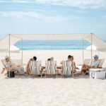 People relaxing under a canopy on a sandy beach with the ocean and sky in the background.