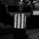 Person standing with arms raised in a room with a sofa and television, black and white image.