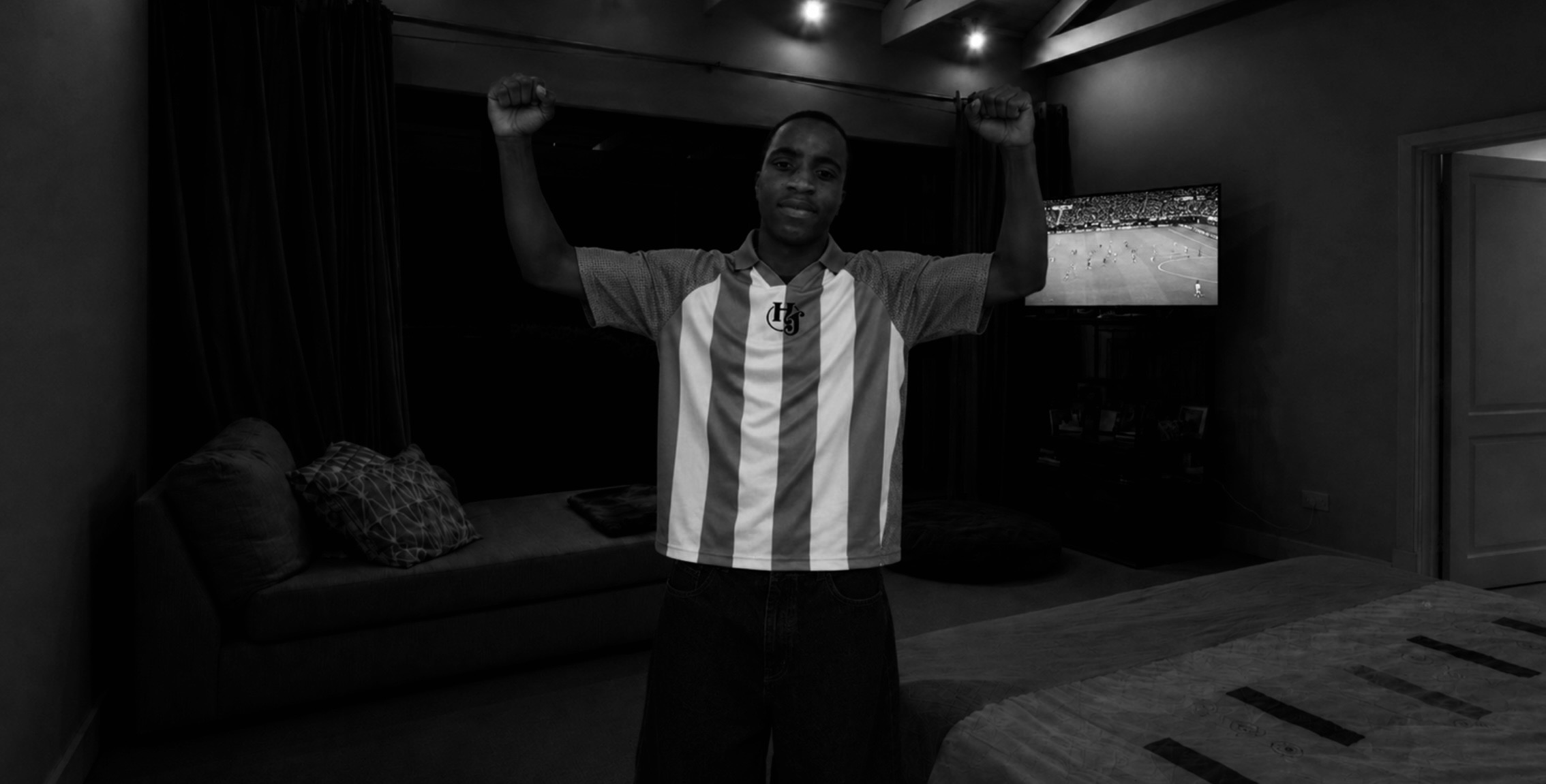 Person standing with arms raised in a room with a sofa and television, black and white image.