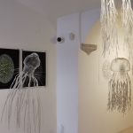 Gallery with three digital art pieces on the wall and hanging decorations resembling jellyfish or sea creatures.