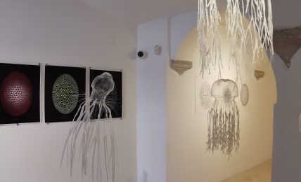 Gallery with three digital art pieces on the wall and hanging decorations resembling jellyfish or sea creatures.