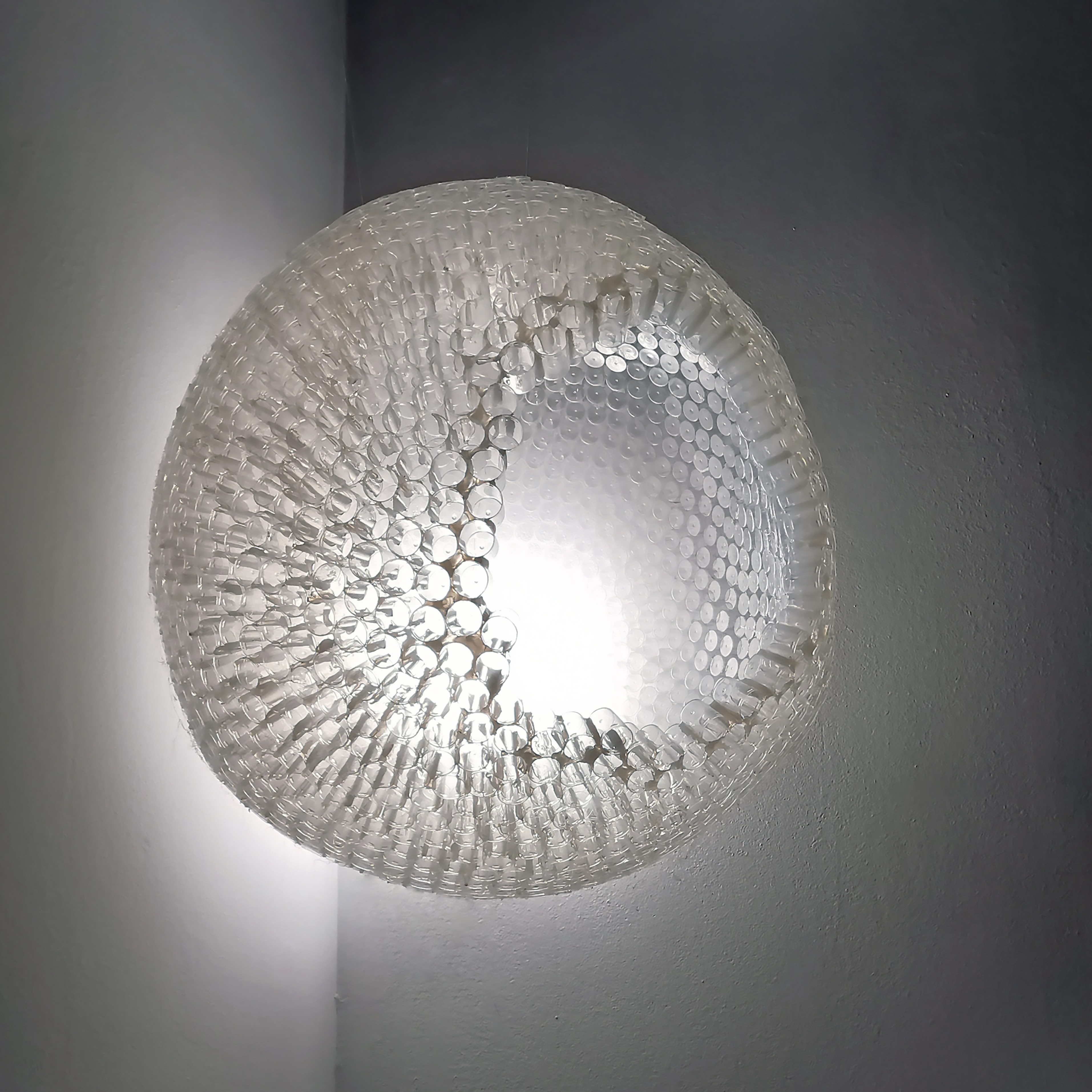 Round textured glass ceiling light fixture with light shining through, mounted on a wall.
