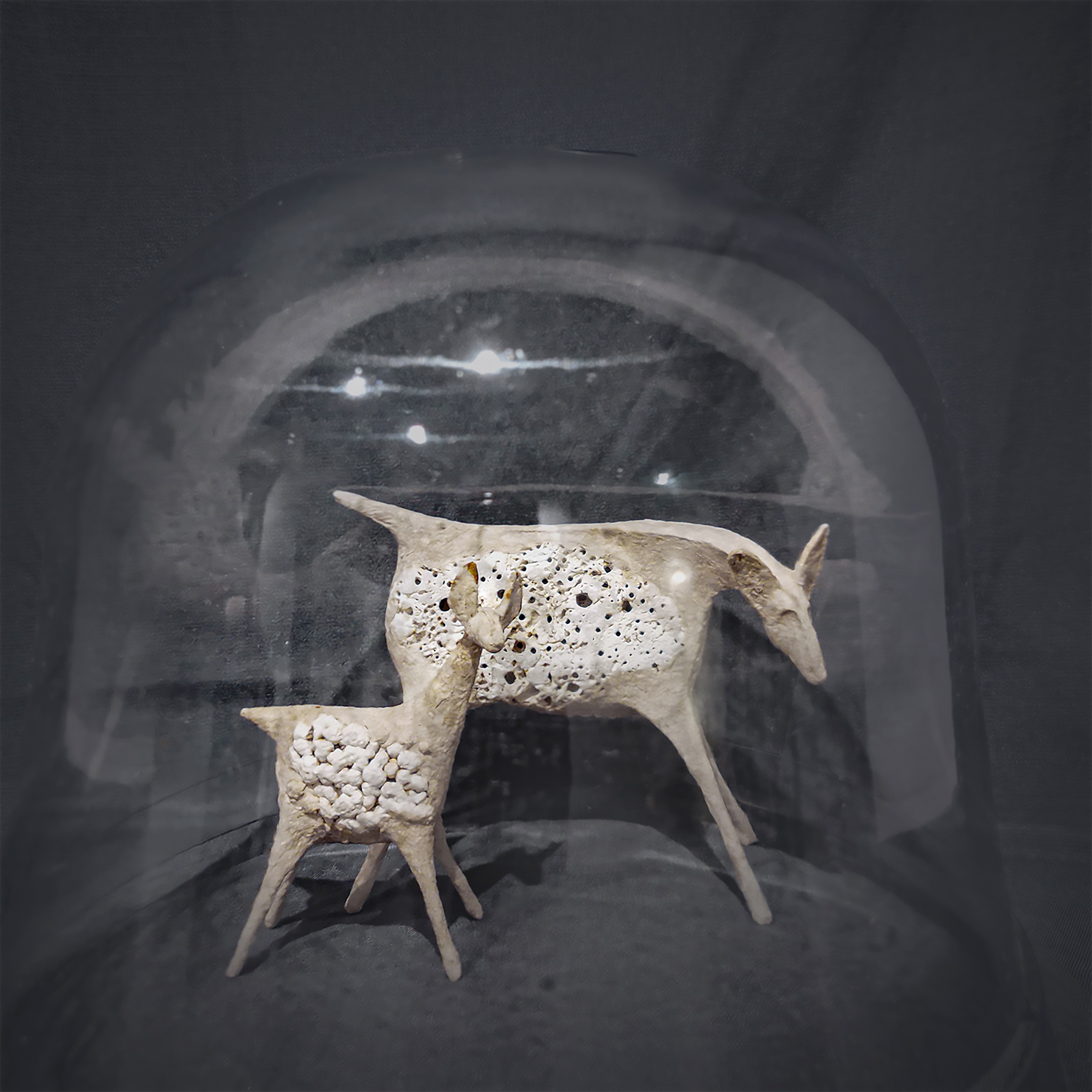 Two ceramic animal sculptures, one resembling a goat and the other a smaller creature, displayed against a dark background.