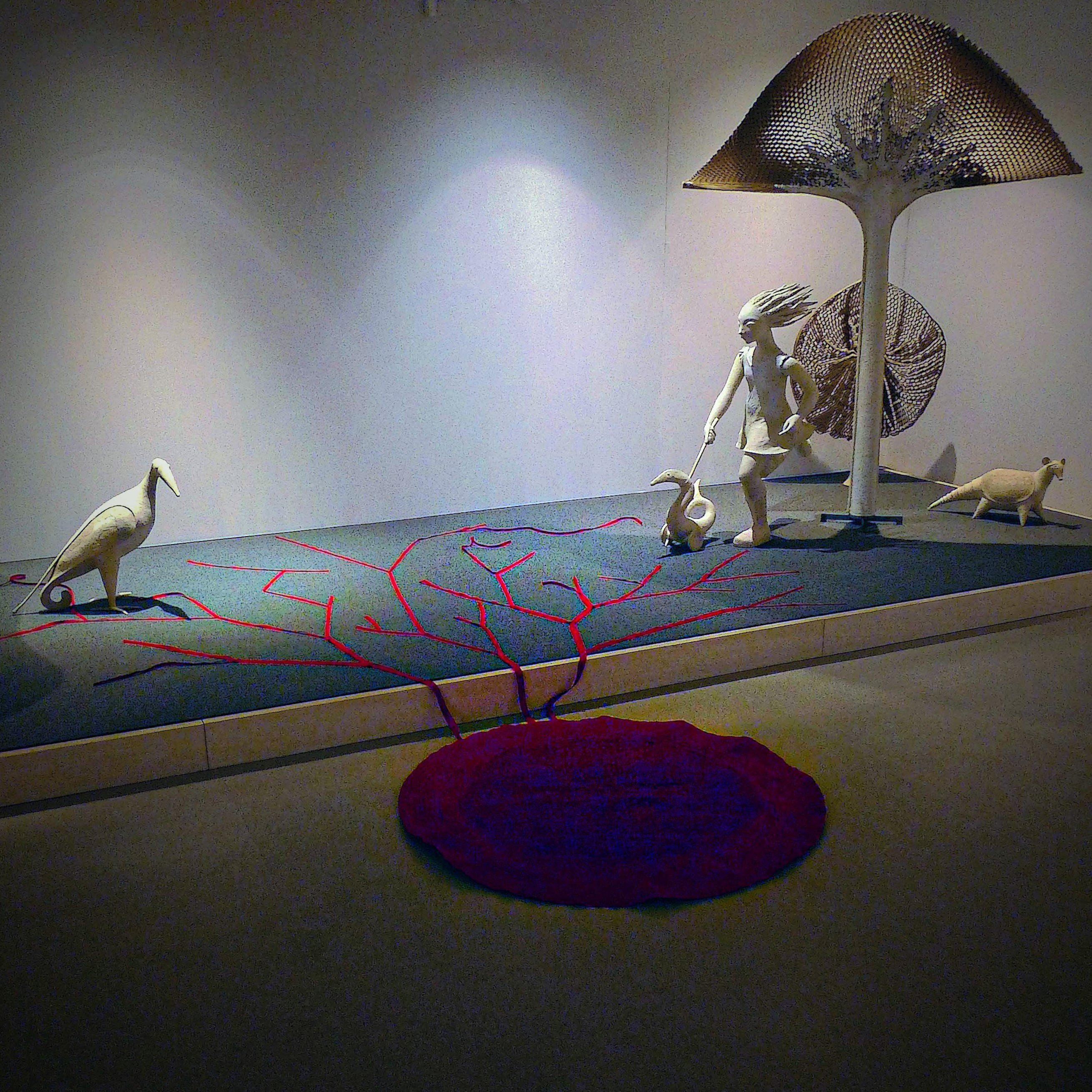 Display with animal sculptures, a child figure, a large mushroom-like structure, and a red circular element on the floor.