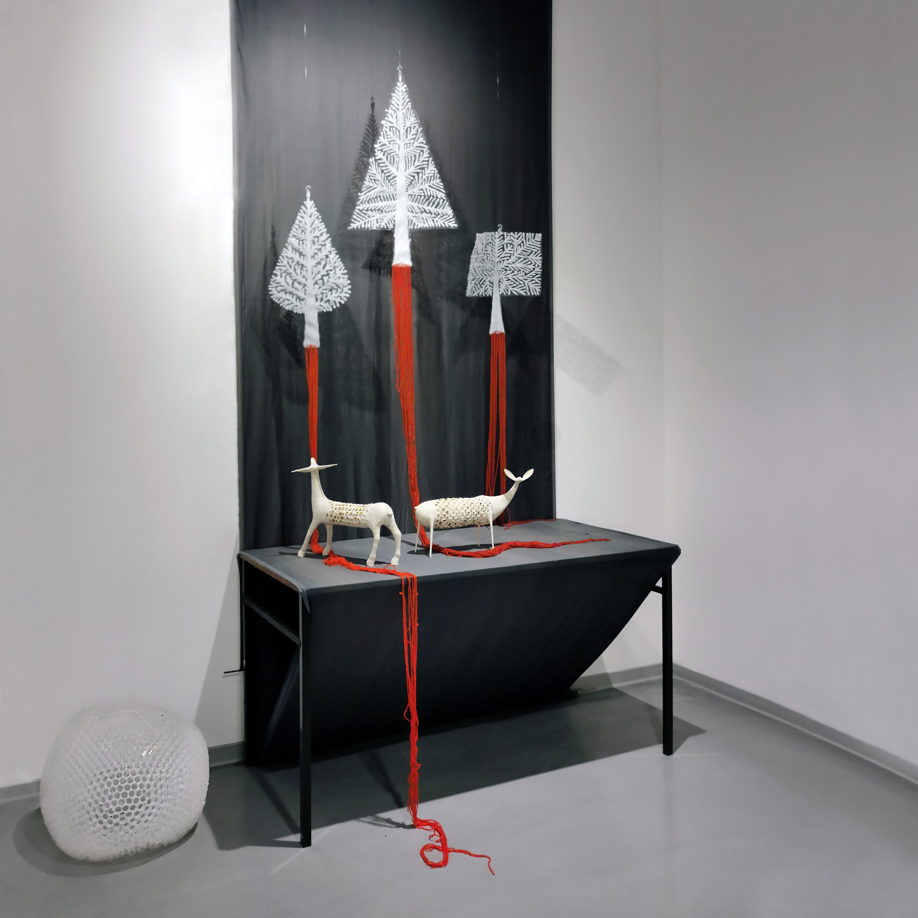 Decorative art display with white reindeer figures, red yarn, and black background, on a black table against a white wall.