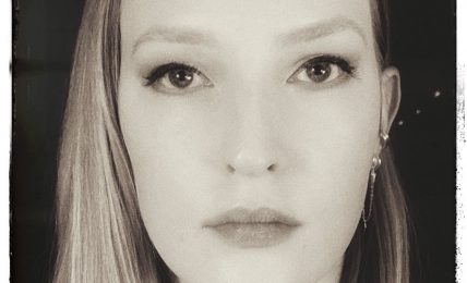 Black and white portrait of a woman with long hair, looking directly at the camera with a neutral expression.