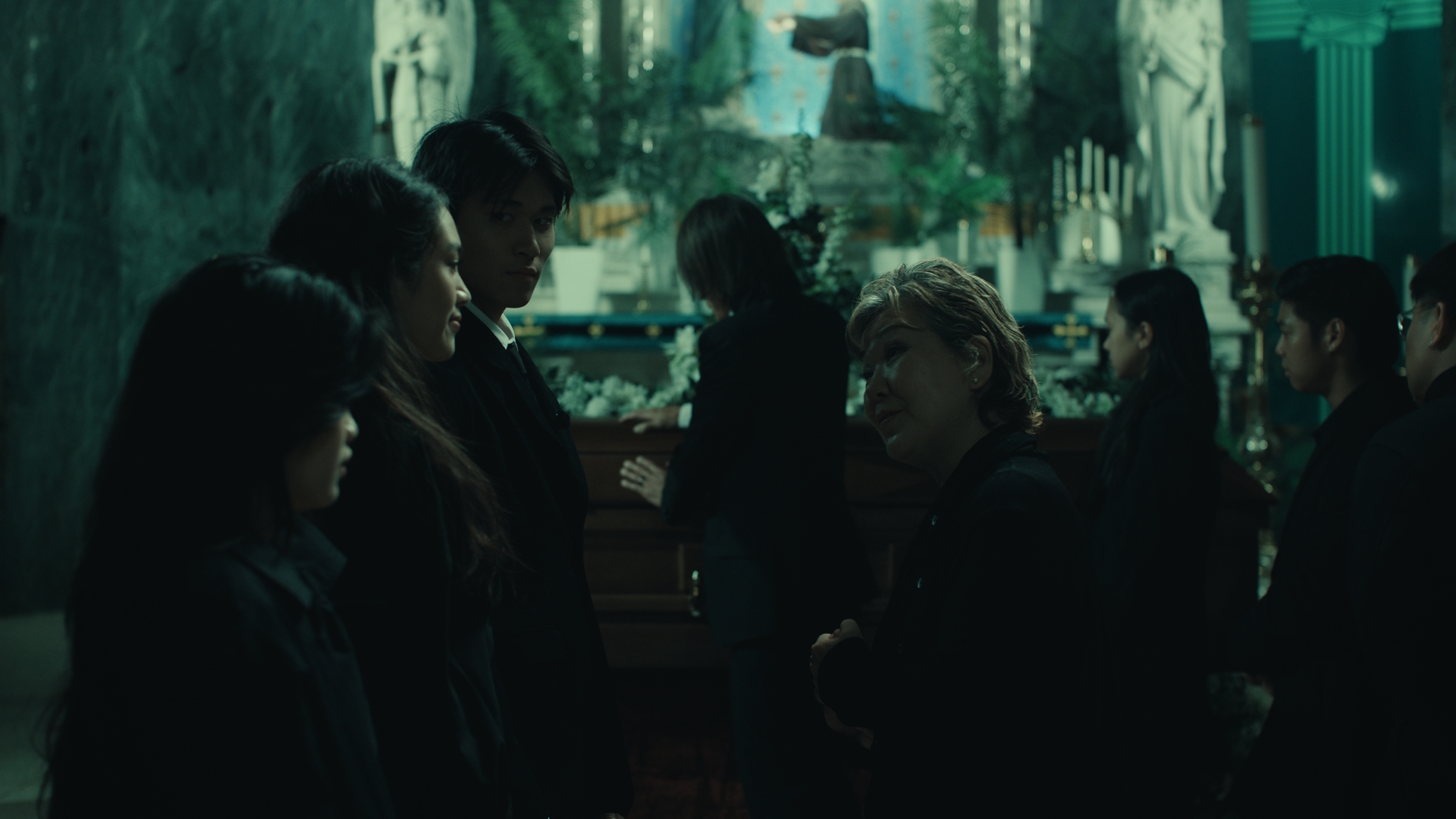 Group of people standing in a dimly lit outdoor area with trees and hanging lights, engaged in conversation.