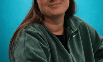 Young woman wearing a black cap and green Nike sweatshirt, smiling against a blue background.