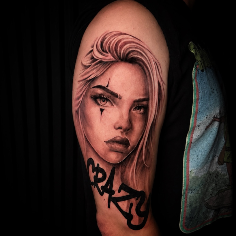 Tattoo of a woman's face with blonde hair and a tear on her cheek on an arm, with the word 'CRAZY' below.