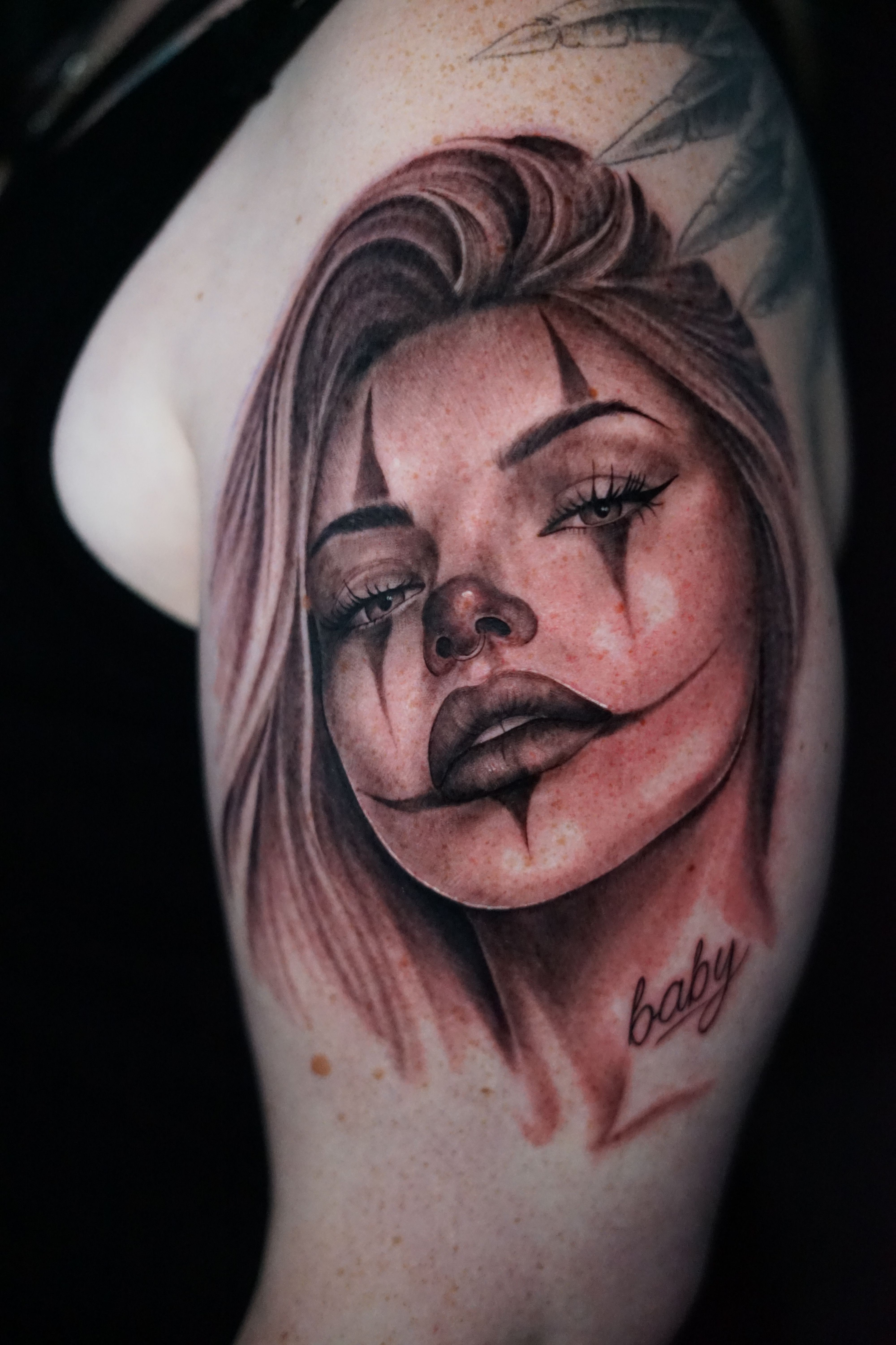 Tattoo of a woman's face with closed eyes and flowing hair on skin, with some text below. 20 words.
