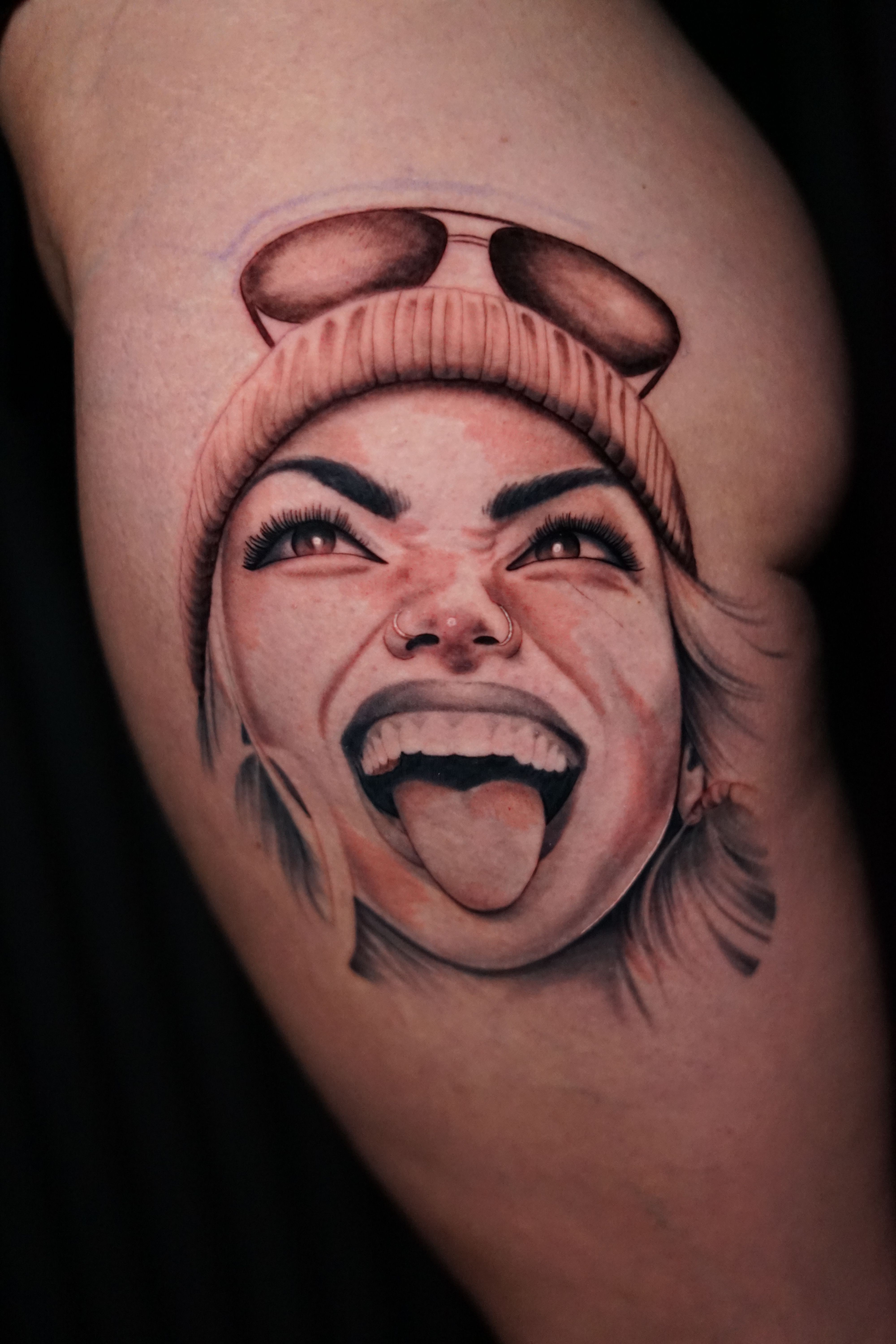 Tattoo of a woman's face with an open mouth, showing her tongue and teeth, on skin. The face appears expressive.