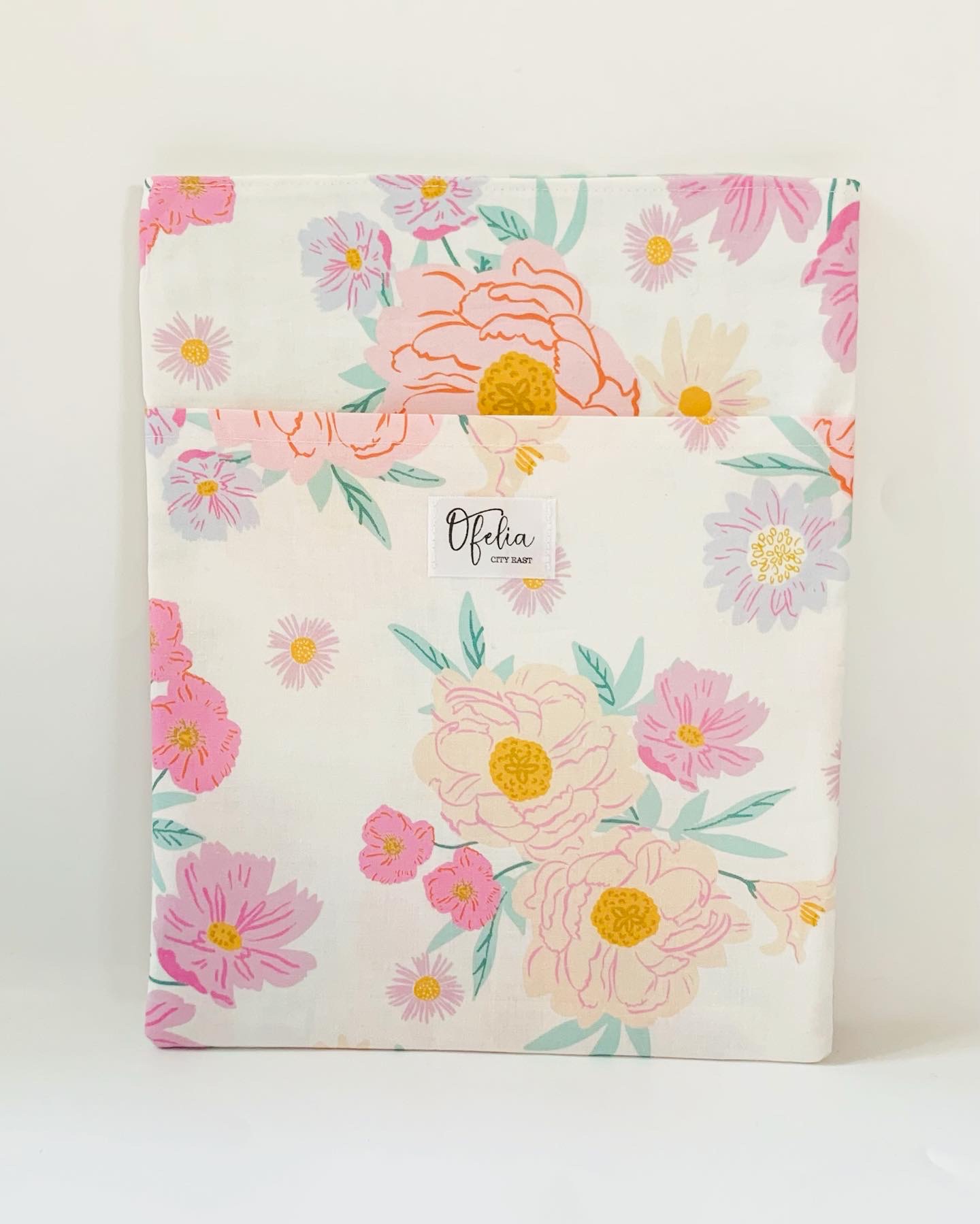Folded floral fabric with pink, yellow, and purple flowers on a white background, label in the center, against a white surface.