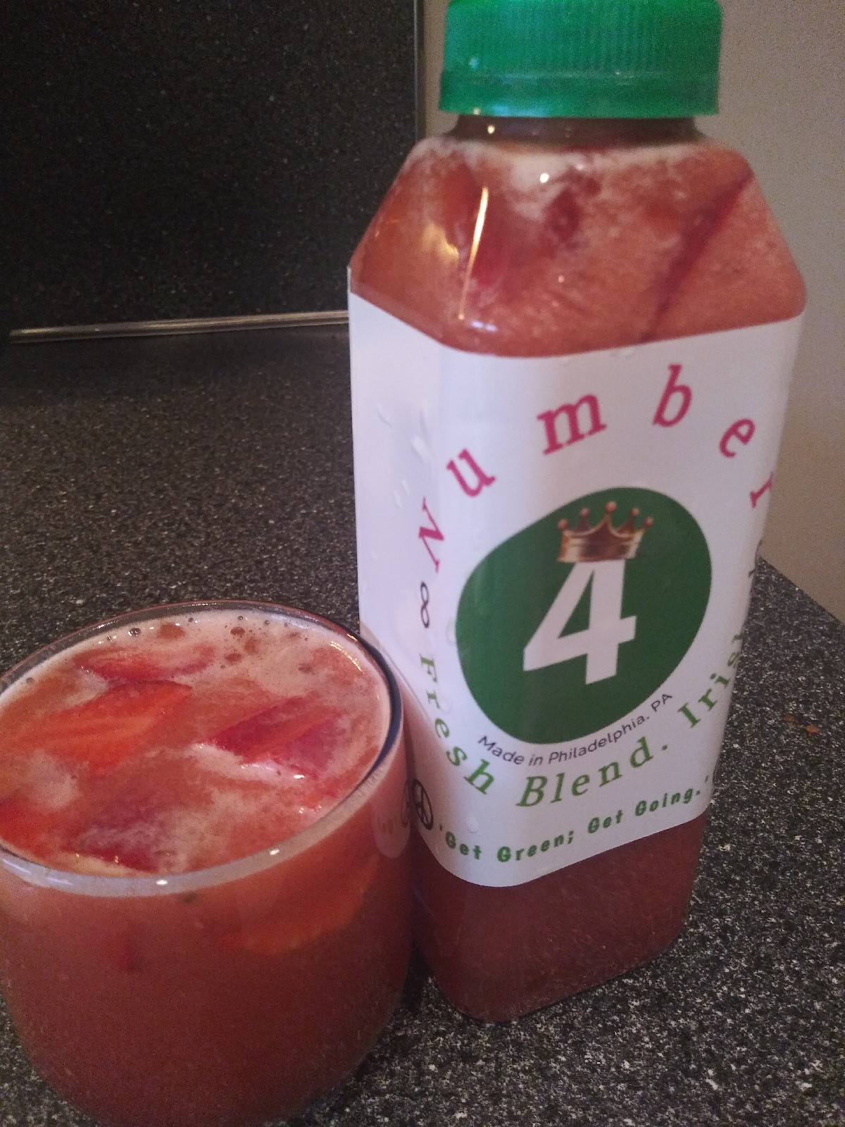 Bottle of watermelon-flavored drink and a glass with the same drink on a black surface.