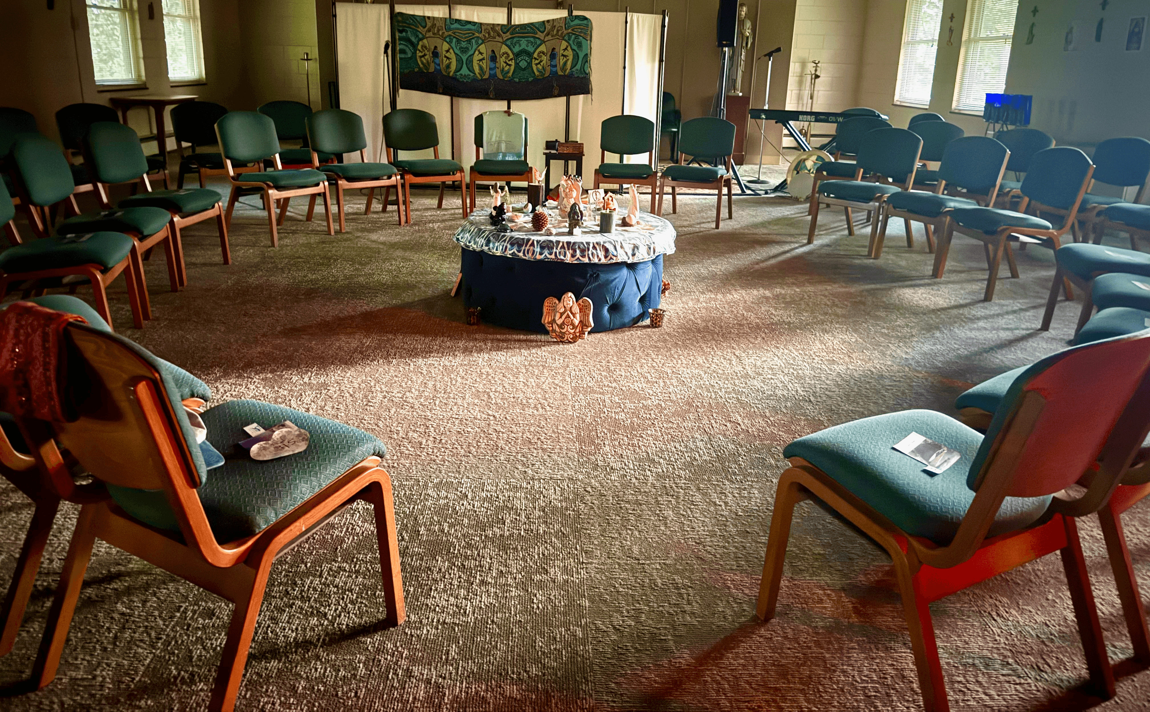 Empty circular room with chairs arranged in a circle, a table with decorations in the center, and windows letting in natural light.