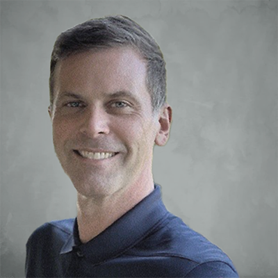 Portrait of a smiling man with short dark hair, wearing a dark collared shirt, against a plain background.